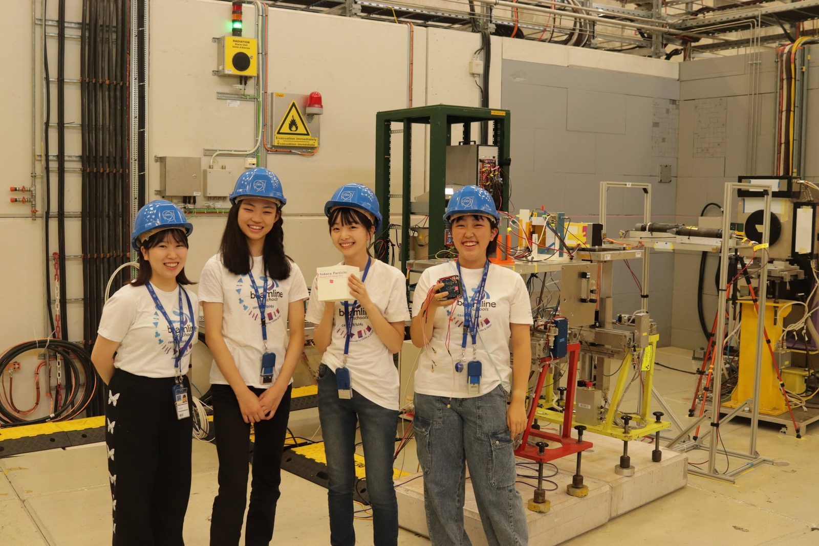 CERN Beam Line for Schools の実験エリアで、ヘルメット姿の女子4人組チーム Sakura Particles が並ぶ