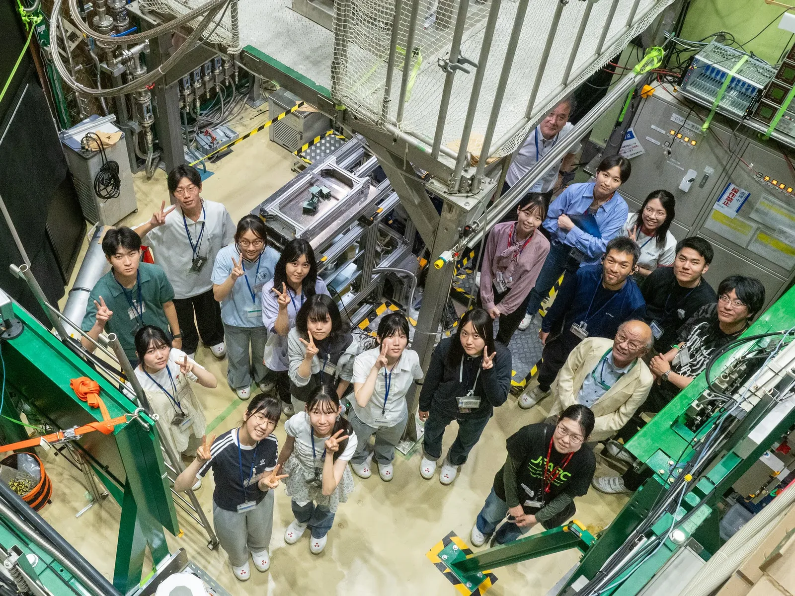 J-PARC ミュオンD1エリアのビームライン前に集まり、実験を行う設備を見上げる参加中高生と加速キッチン・KEKのスタッフ